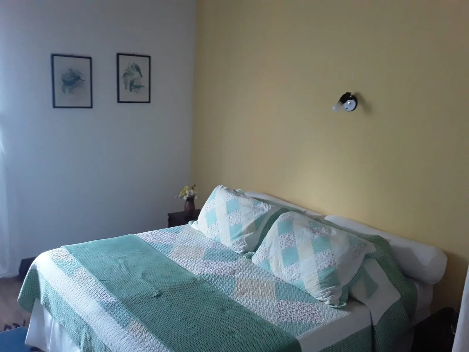 Apartamento de casal com colcha em tons de verde e janela lateral
