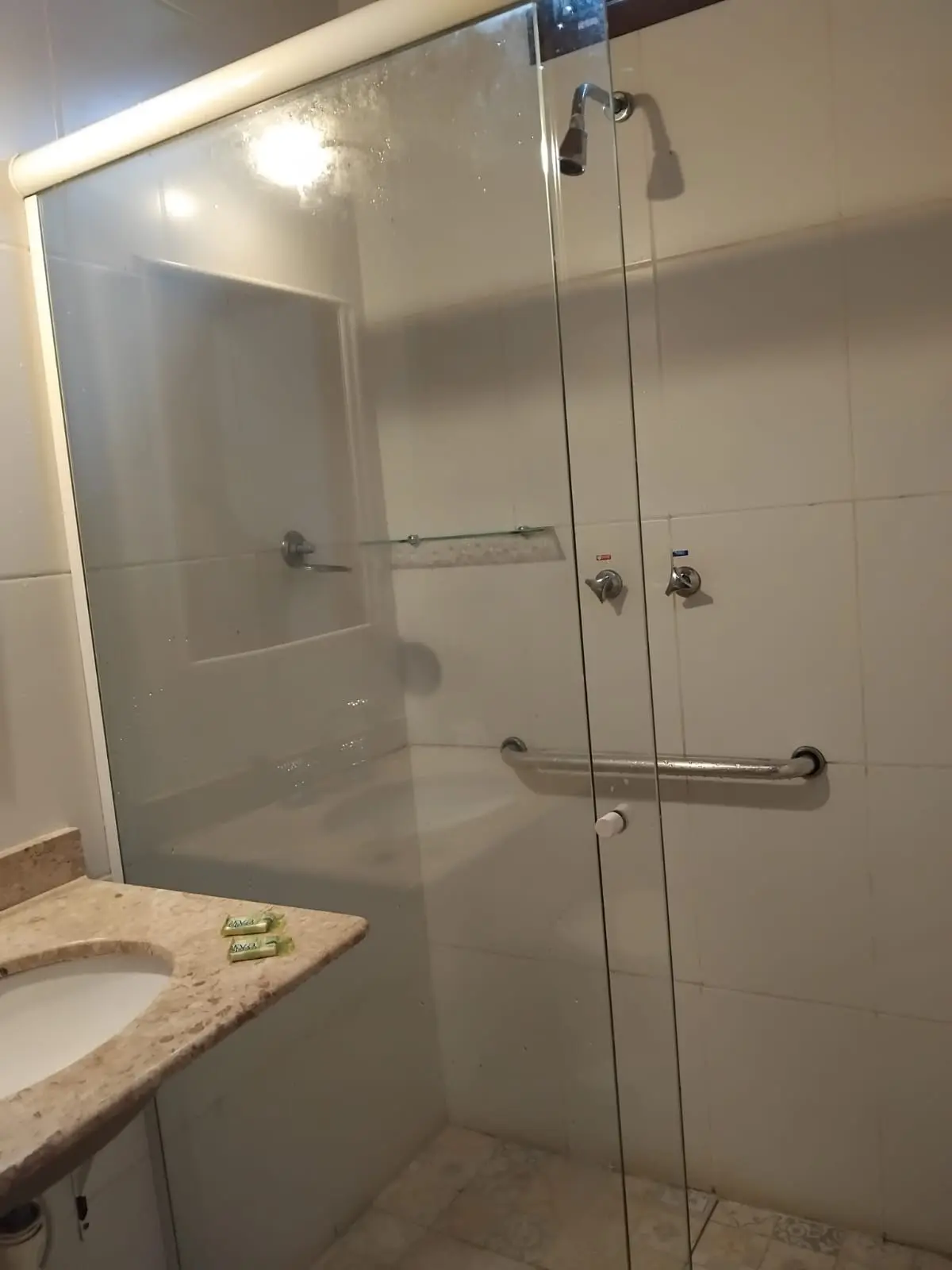 Banheiro de apartamento com boxe de vidro, lavatório e apoio de segurança