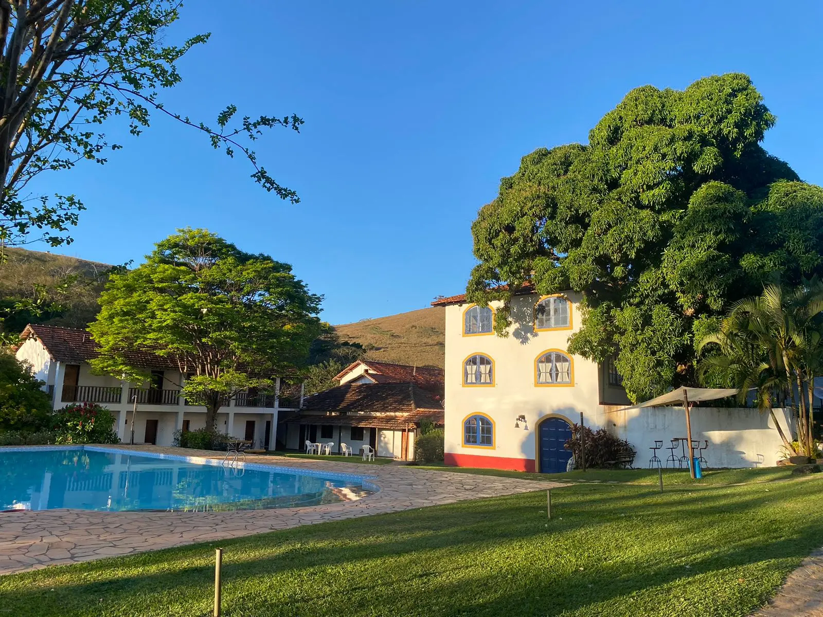 Piscina, jardim e edifícios do hotel em dia de céu azul